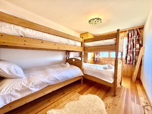 Quarto com beliches, paredes de madeira e um tapete branco e fofo.