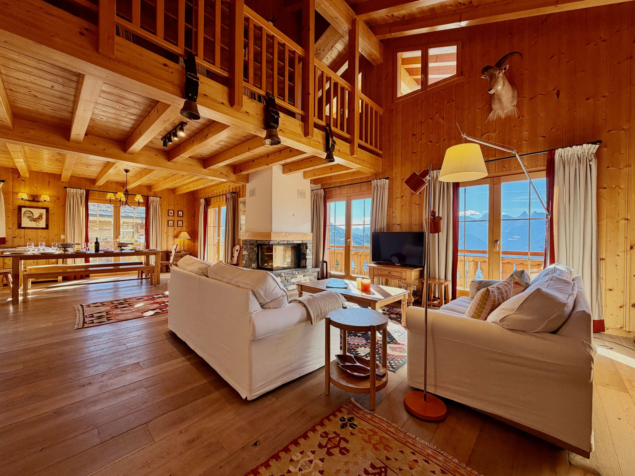 A spacious wooden interior with a fireplace, seating area, and a balcony with a mountain view.