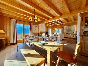 Interior em madeira com uma mesa de jantar posta para quatro pessoas, um sofá e uma lareira.