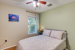 A bedroom with a bed, a ceiling fan, a window with curtains, a painting on the wall, and a nightstand with a lamp. - Easy Airport Access! Austin Home w/ Patio (Austin)