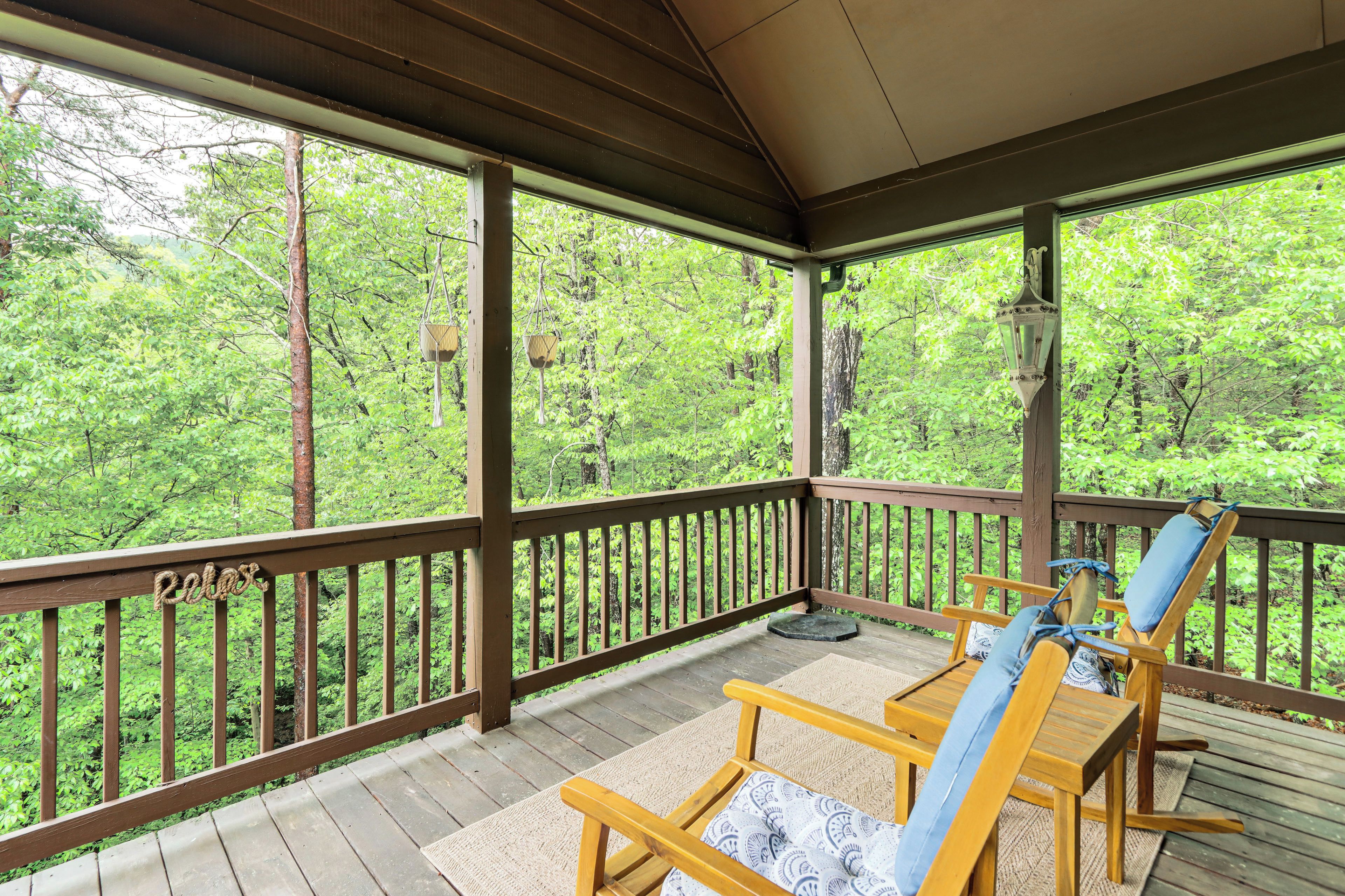 A covered outdoor deck with wooden furniture and a view of a forest.