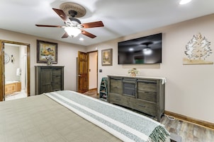 Quarto com cama, ventilador de teto, televisão e cômoda.