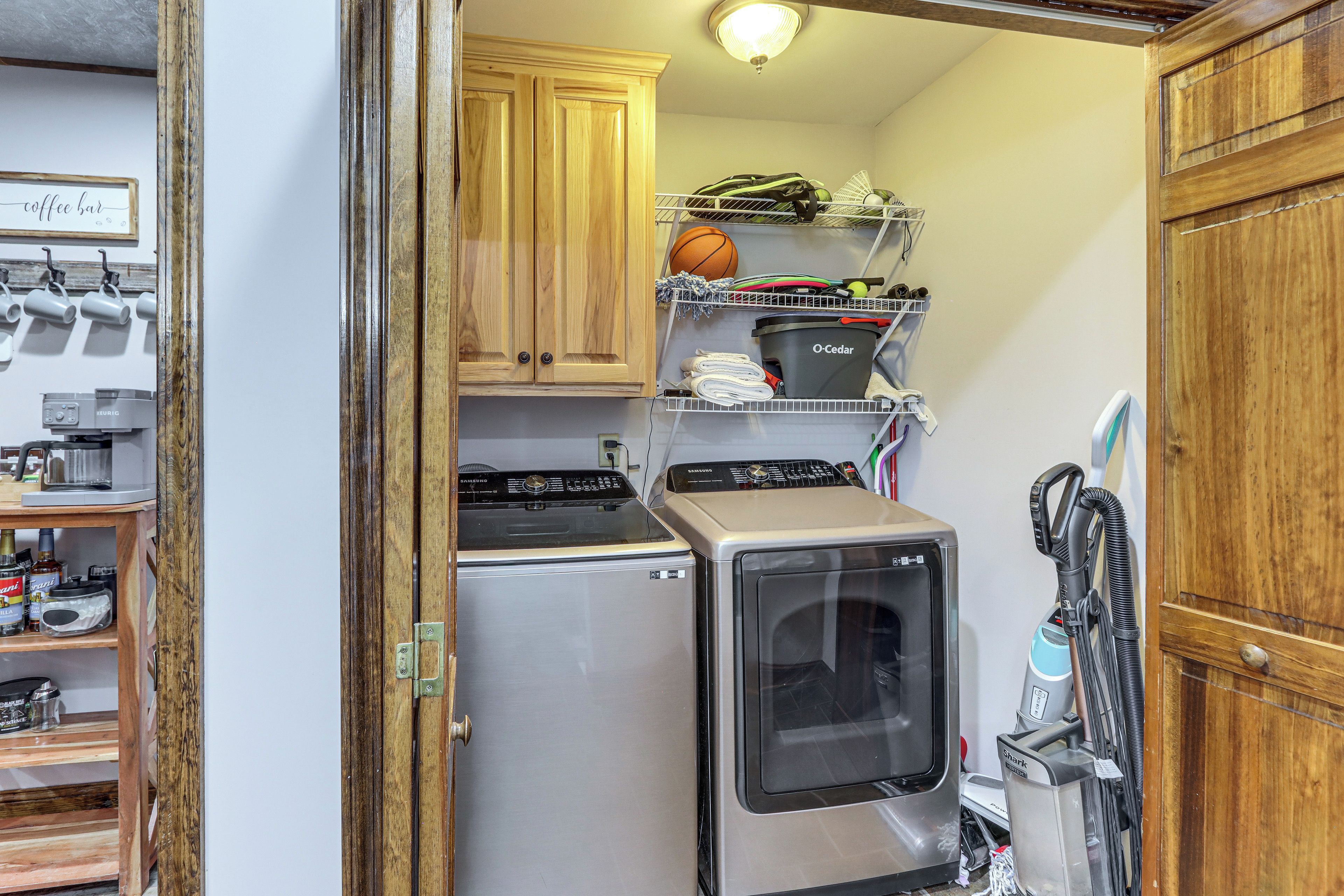 Cocina compacta equipada con refrigerador, horno y microondas. Se observa una repisa con diversos objetos y una aspiradora.