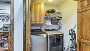 Cocina compacta equipada con refrigerador, horno y microondas. Se observa una repisa con diversos objetos y una aspiradora.