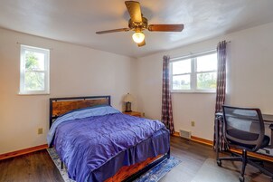 Un dormitorio con cama, escritorio, silla, ventilador de techo y ventana.