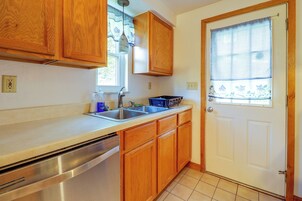Cocina con armarios de madera, lavavajillas de acero inoxidable, un fregadero y una ventana con cortina.