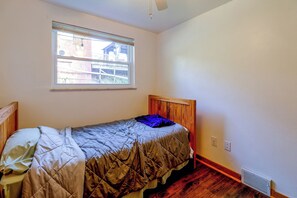 Ein Einzelbett mit Kopfteil, ein Fenster mit Jalousien und ein Deckenventilator.