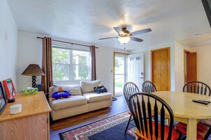 Una habitación con sofá, mesa de comedor con sillas, ventilador de techo y ventana con cortinas.