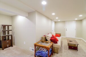 Una habitación con un sofá, una mesa de centro de vidrio, una mesita de noche de madera y una puerta.