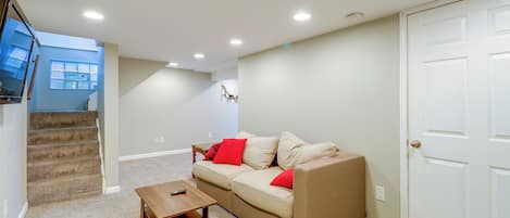 Uma sala de estar com um sofá bege, uma mesa de centro de madeira e uma escada que leva a um andar superior.