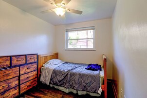 Una habitación pequeña con una cama individual, cabecera de madera, ventilador de techo y ventana que proporciona luz natural.