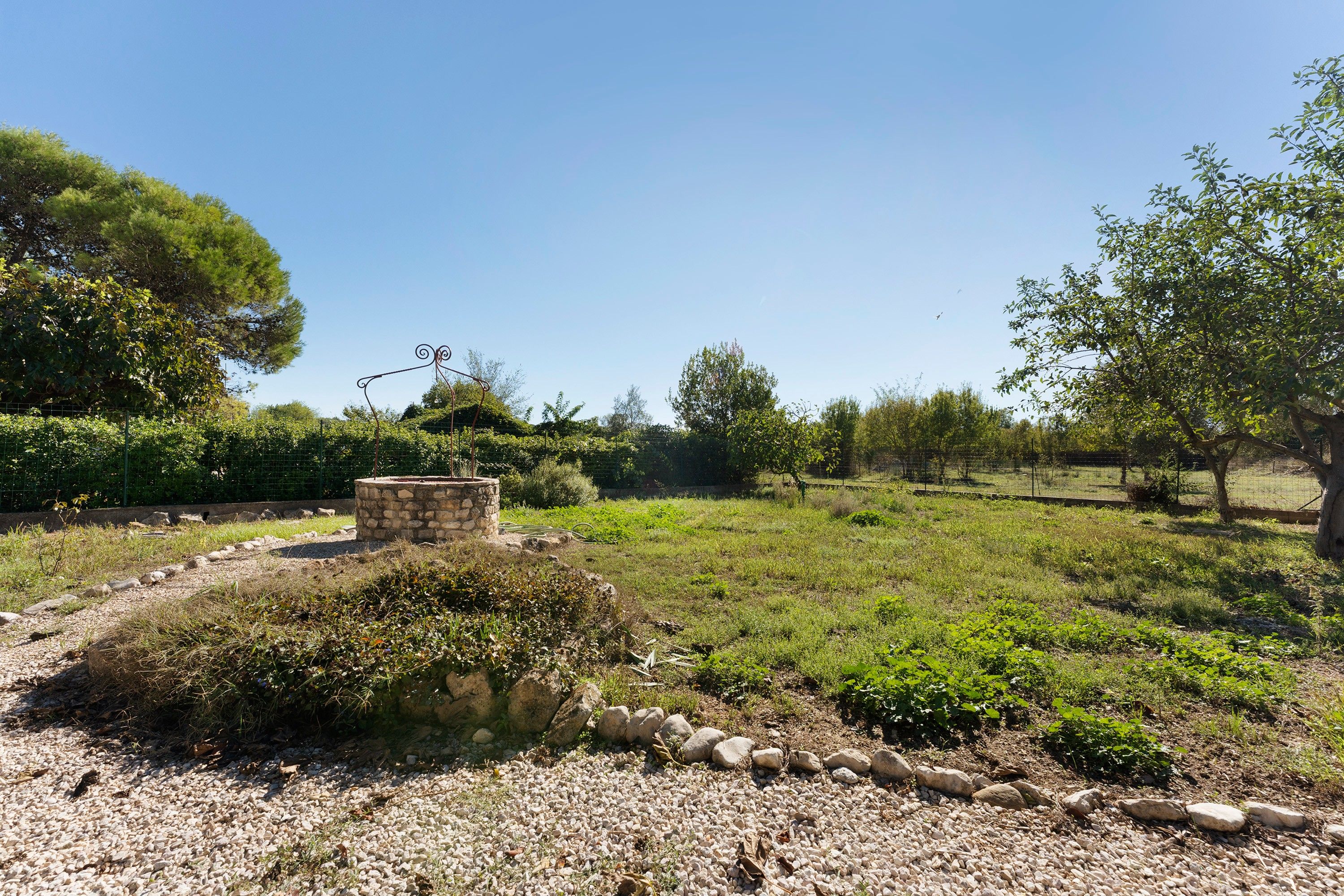 Un jardin agrémenté d’une structure en pierre, d’un chemin de gravier et de diverses plantes.