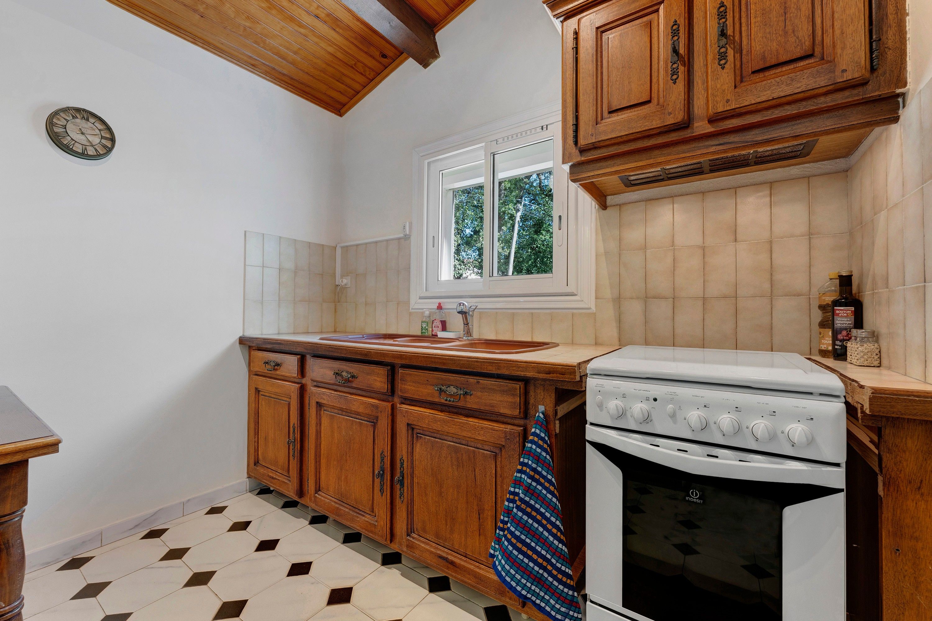 Une cuisine avec des meubles de rangement en bois, un fourneau blanc et une fenêtre donnant sur les arbres.