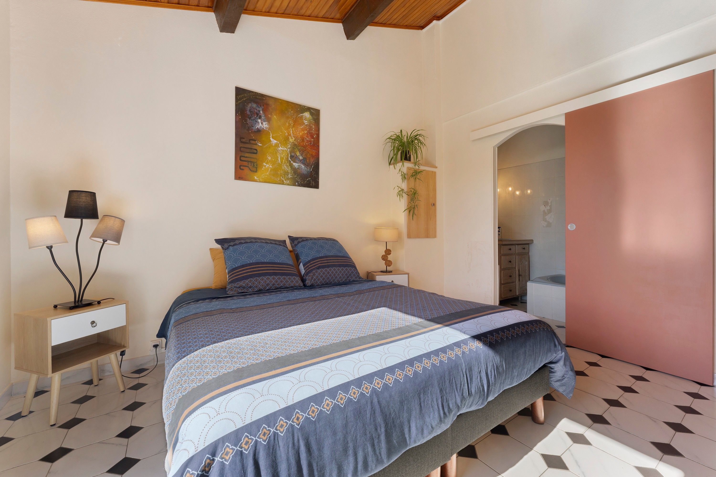 A bedroom with a bed, bedside tables, a wall-mounted plant, and a door leading to a bathroom.