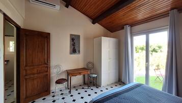 A bedroom with a bed, a wooden door, a white wardrobe, a desk with a chair, and a window with curtains.
