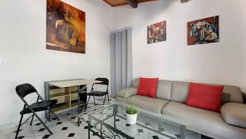 Un salon moderne avec une table basse en verre, un canapé avec des coussins rouges, un coin repas avec une table et des chaises, et des œuvres d’art accrochées aux murs.