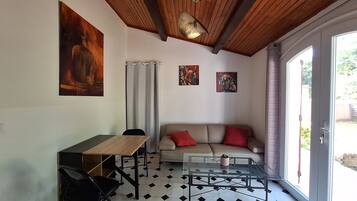 A room with a wooden ceiling, a glass table, a sofa with red cushions, and a dining area with a chair and table.