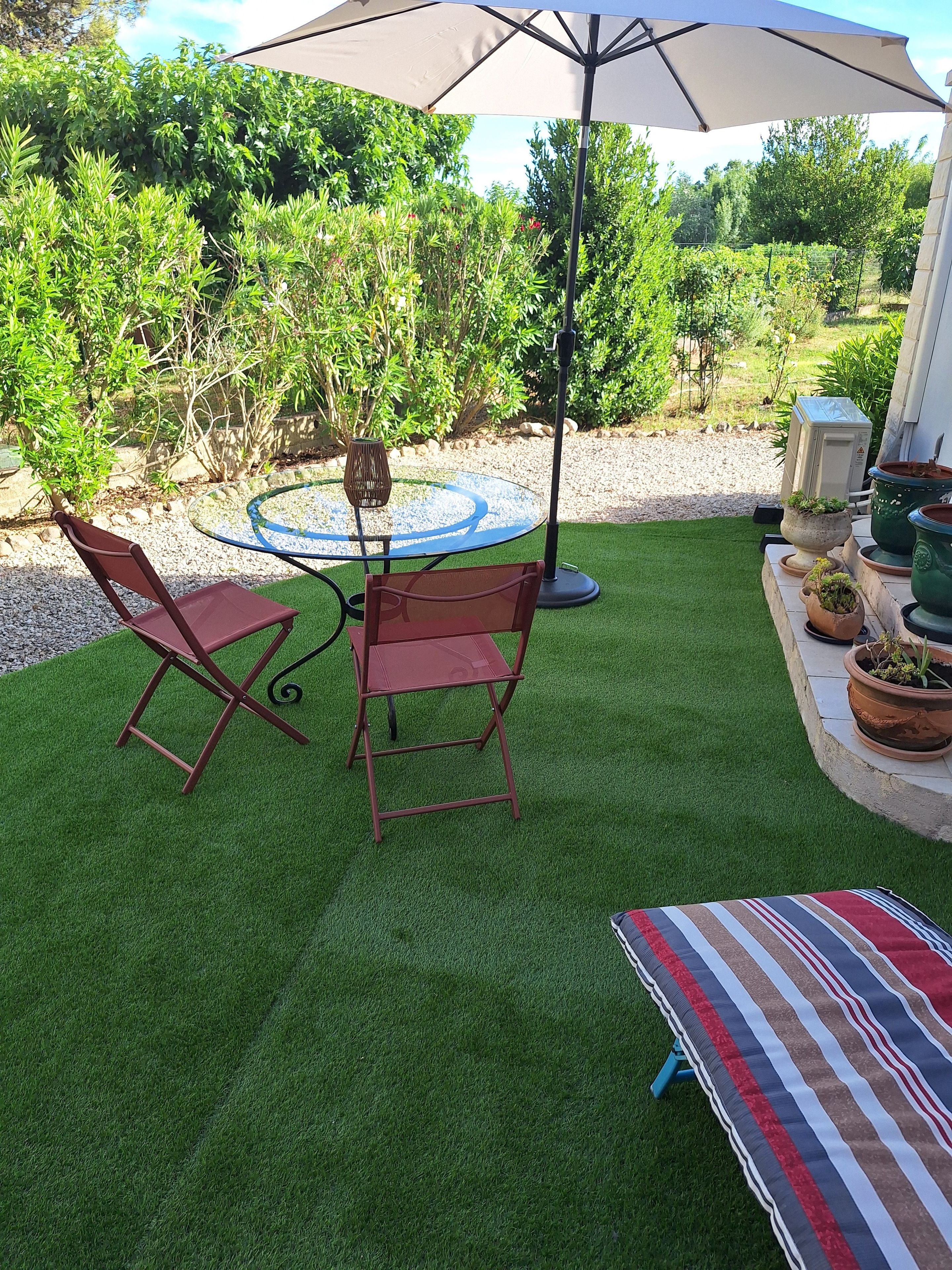 A patio with a round table and two chairs, an umbrella, and potted plants.