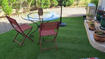 A patio with a round table and two chairs, an umbrella, and potted plants.
