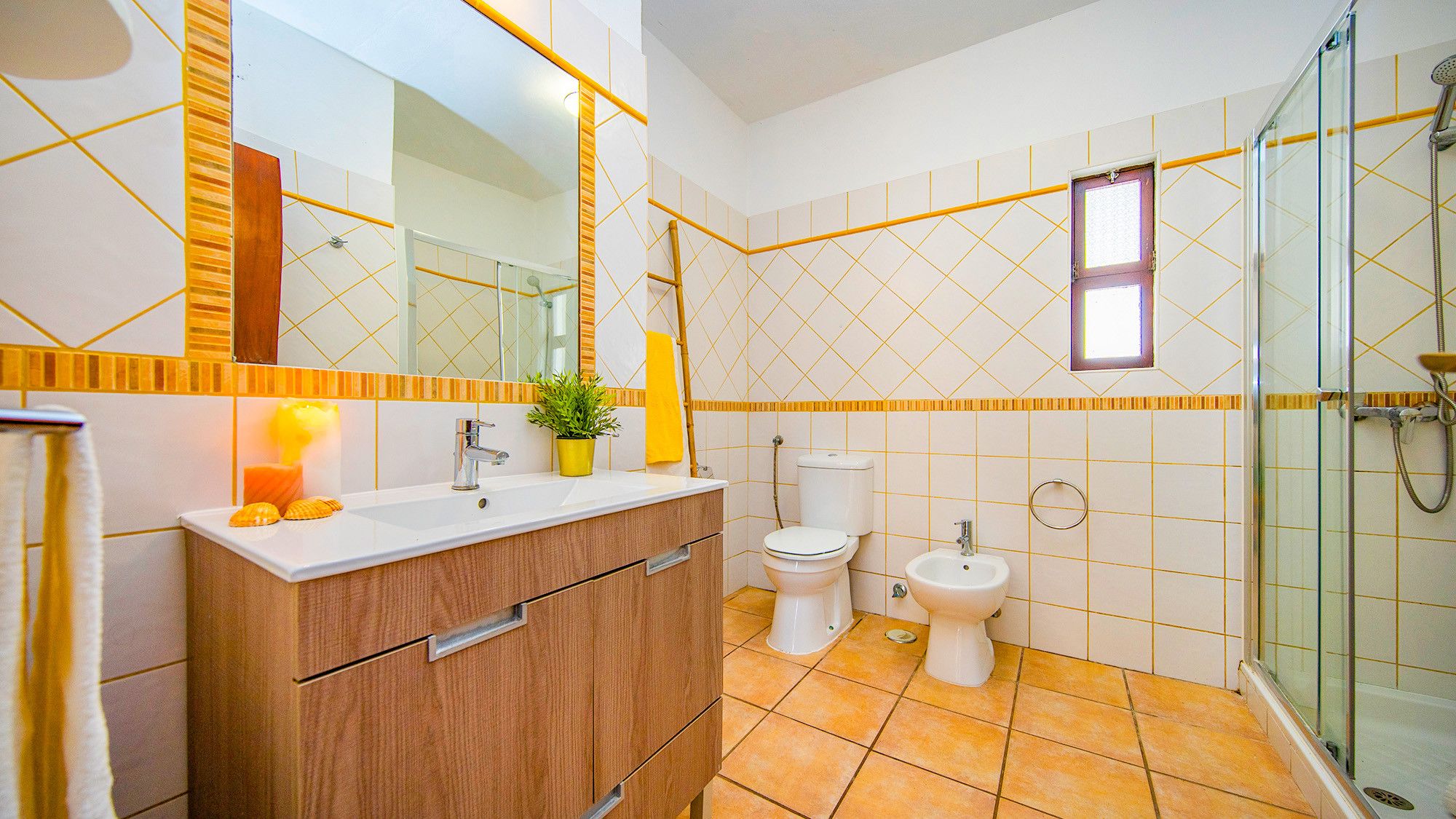 Un baño con tocador de madera, dos inodoros, cabina de ducha con mampara de vidrio y espejo con marco amarillo.