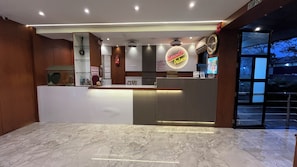 Zona de recepció d'un hotel amb sòl de marbre, un taulell de recepció, un rellotge i un cartell que diu 'Sanwich Place'.