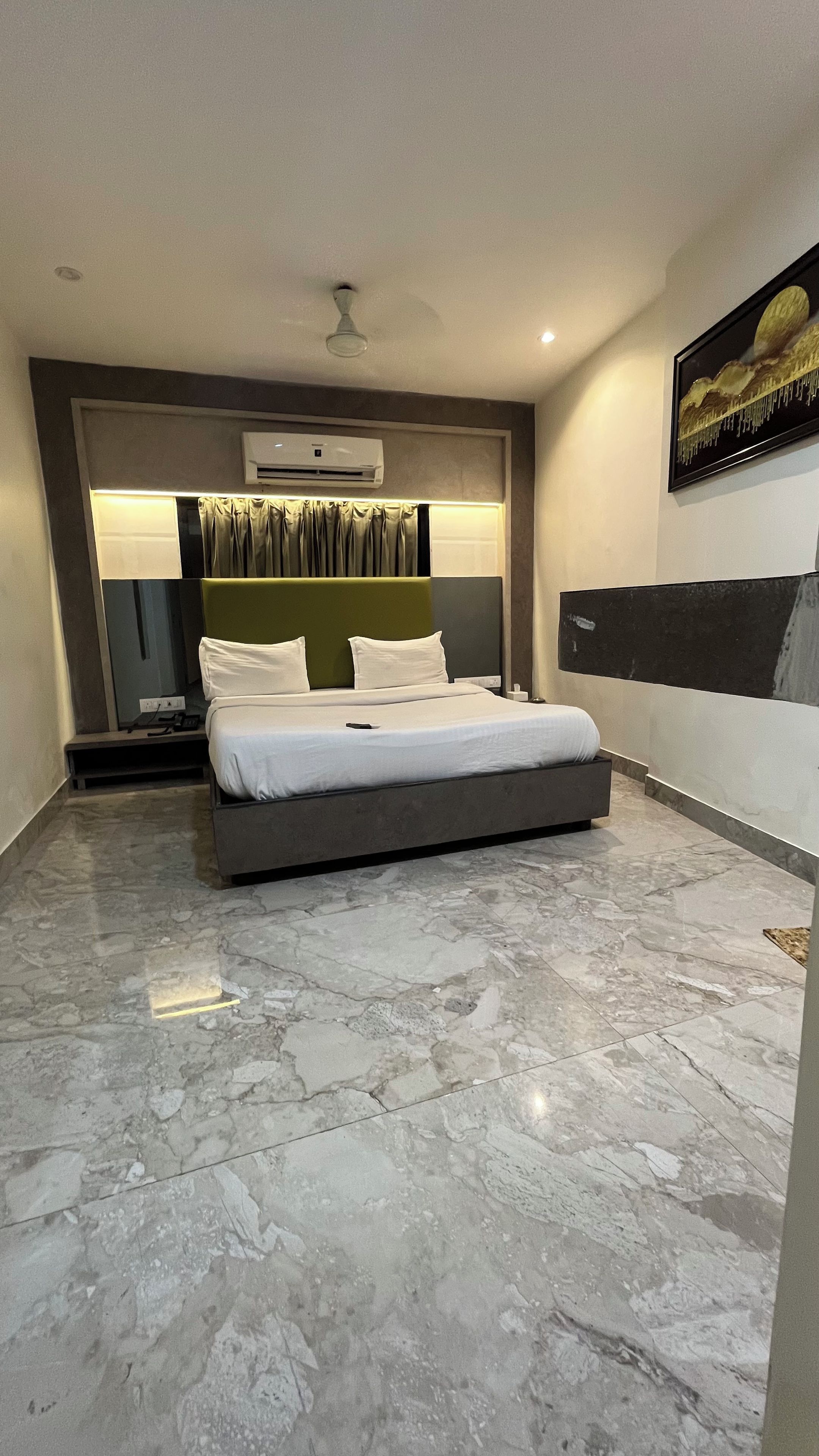 Un dormitorio moderno con una cama grande, un equipo de aire acondicionado, una mesita de noche y una obra de arte en la pared.