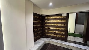 Une pièce d’angle avec un sol en marbre, un mur foncé à motifs et une fenêtre avec des stores.