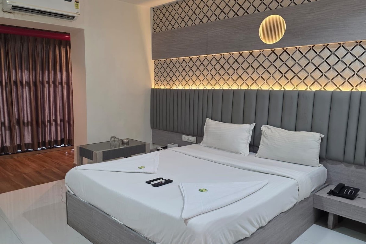 Une chambre d’hôtel moderne avec un grand lit, des tables de chevet, un bureau et un plafond décoré de motifs.
