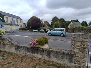 A parking area with a blue car, a stone wall, and a building with a sign. - Maison cosy avec terrasse • Proche Nantes (Vigneux-de-Bretagne)