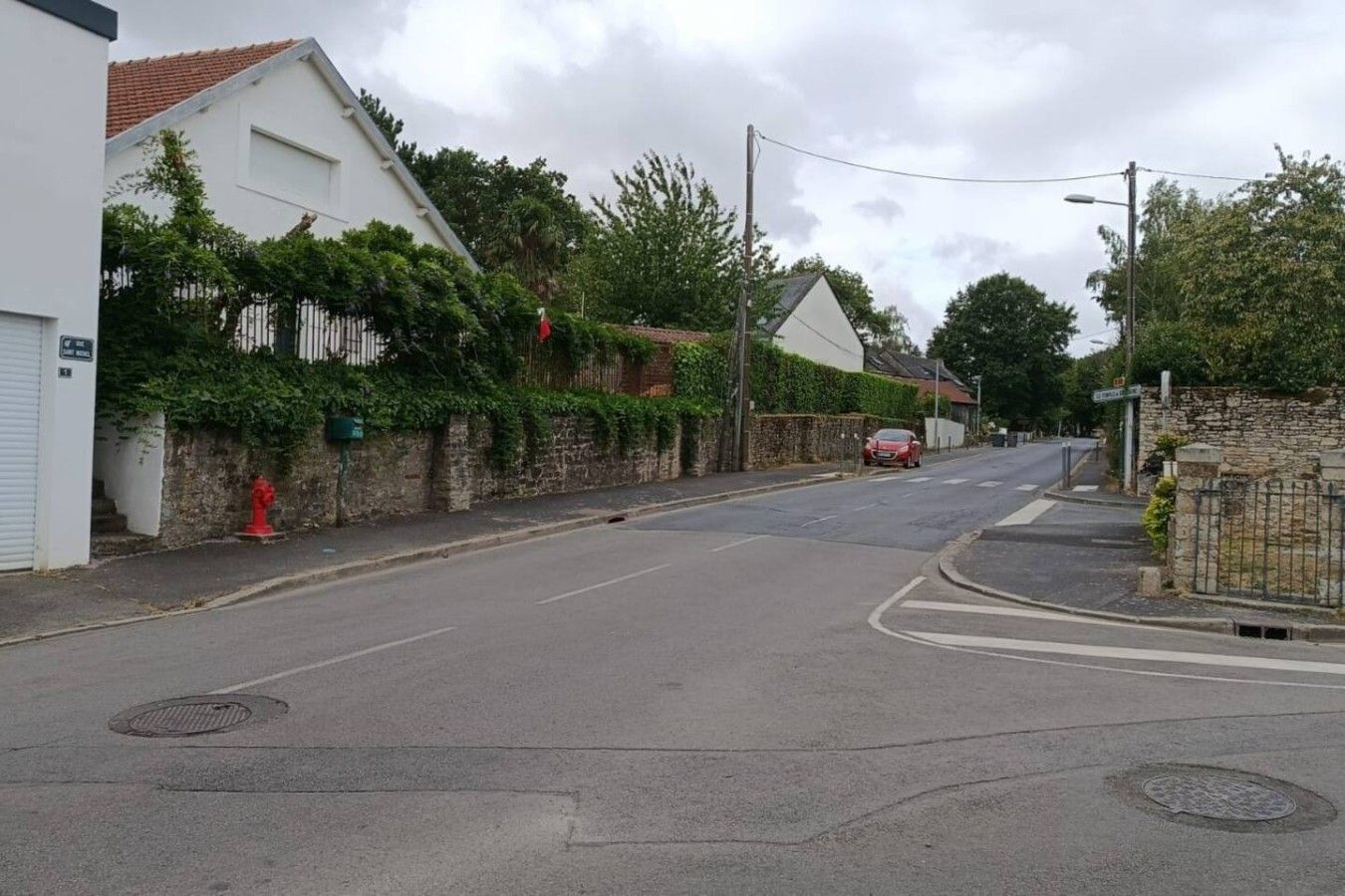 Eine ruhige Wohnstraße mit Häusern, einem roten Hydranten und einem am Straßenrand geparkten Auto.