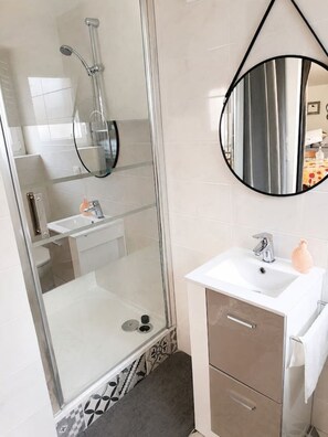 A modern bathroom with a glass-enclosed shower, a white sink, and a round mirror.