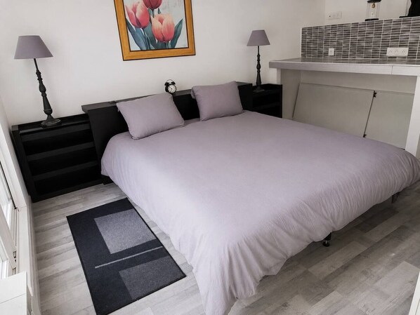 Une chambre à coucher comprenant un lit, deux tables de chevet, une petite table, une lampe, un tableau et un mur recouvert de carreaux.