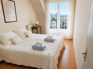 A bedroom with two beds, a radiator, a nightstand, and a view through a window. - All on foot • Private parking • 2 bedrooms (Le Pouliguen)