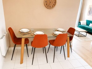 Ein Essbereich mit einem Glastisch, vier orangefarbenen Stühlen und einer Holz-Wanduhren.