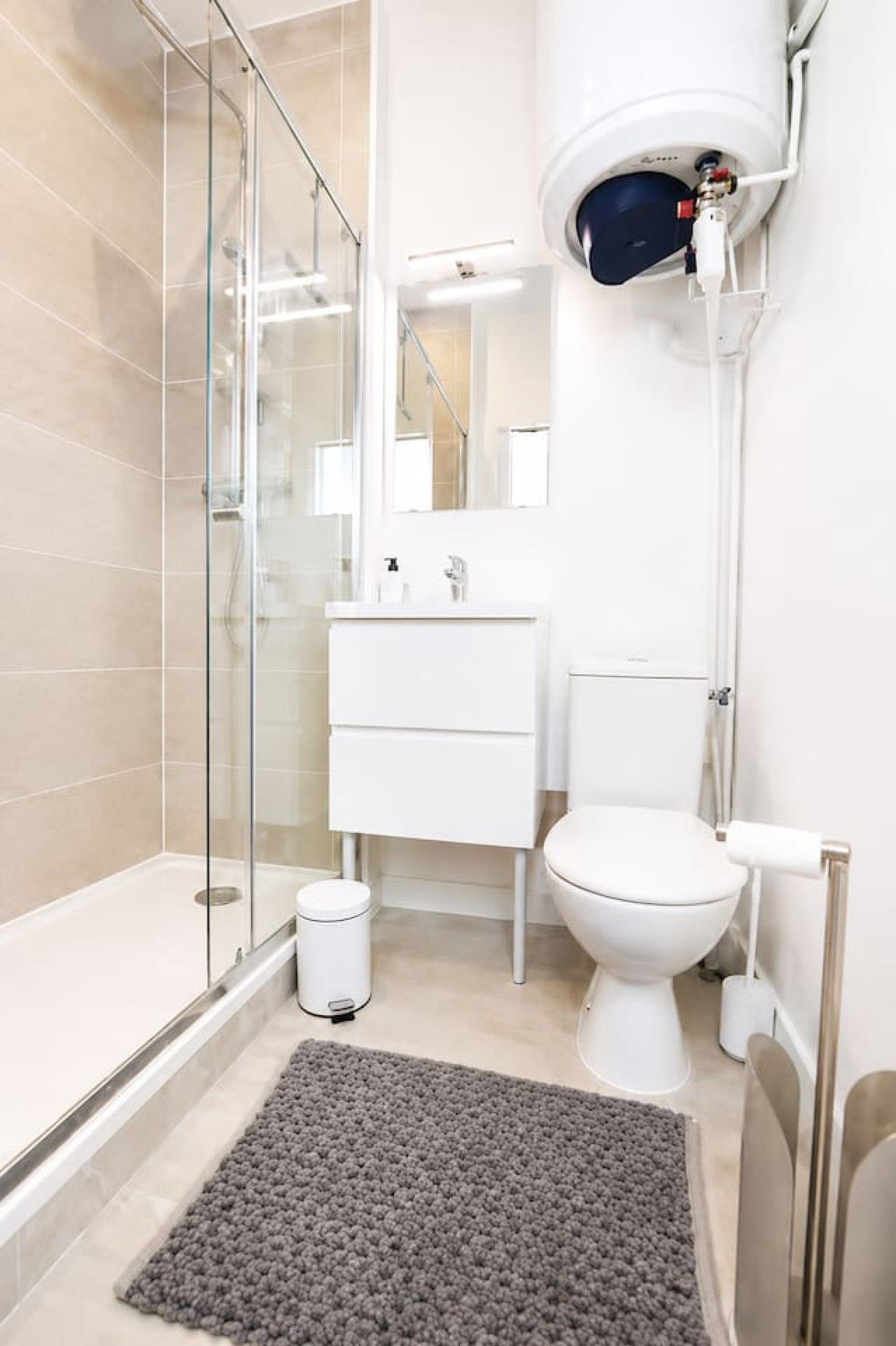 Une salle de bain moderne avec une douche à parois de verre, des toilettes blanches et un lavabo surmonté d’un miroir.