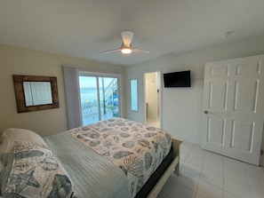A bedroom with a bed, a ceiling fan, a television, and a door leading to a balcony with a view of the sea. - Manasota Key Waterfront Condo Full Kitchen 1 Bed Boat Dock Beach Access Kayaks (Englewood)