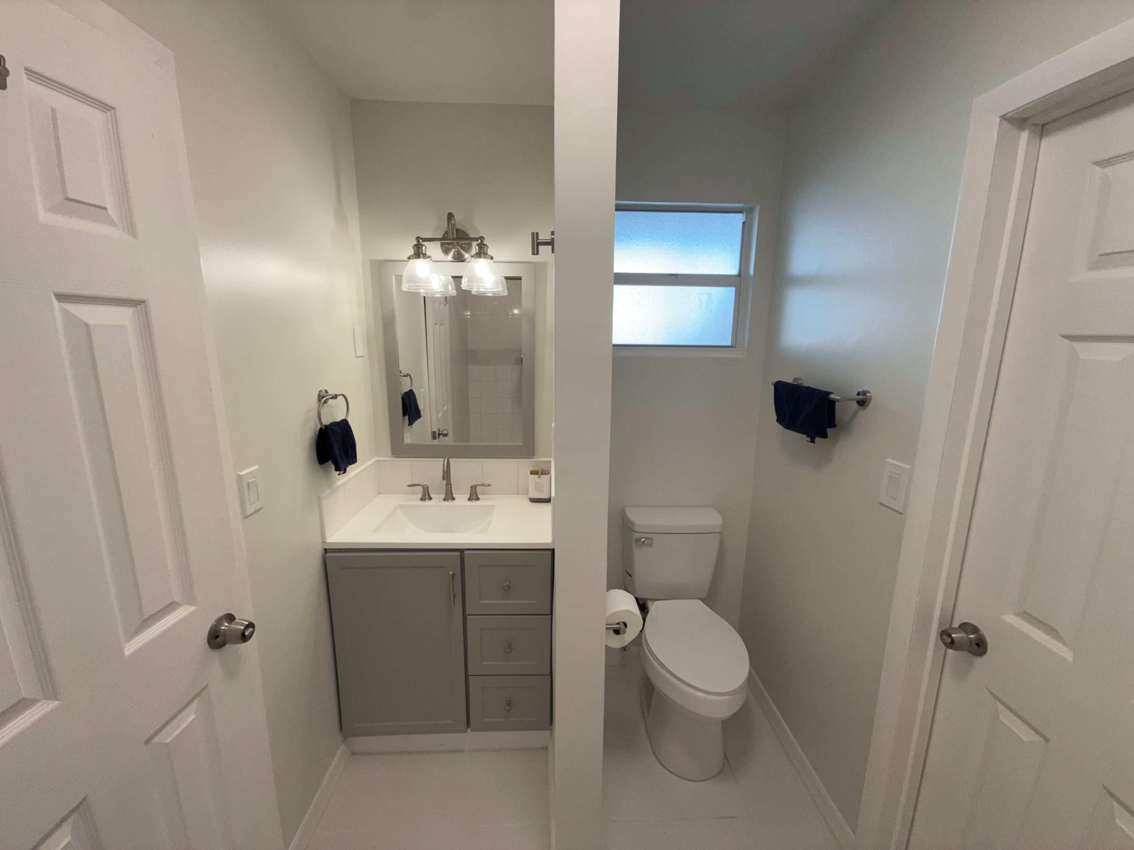 Een kleine badkamer met een witte wastafel, een toilet en een spiegel boven de wastafel.