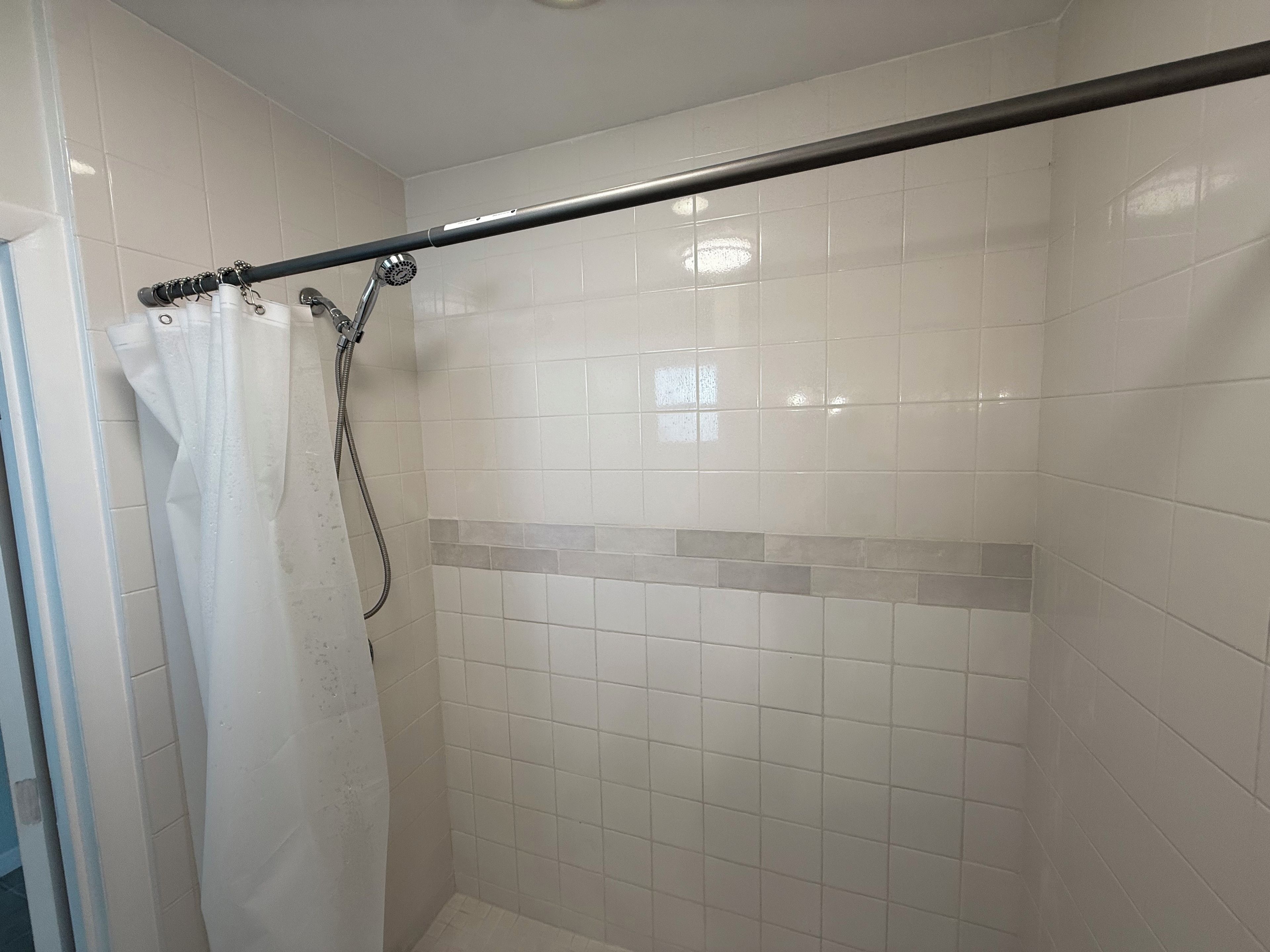 A shower area with white tiles, a showerhead, and a curtain rod.