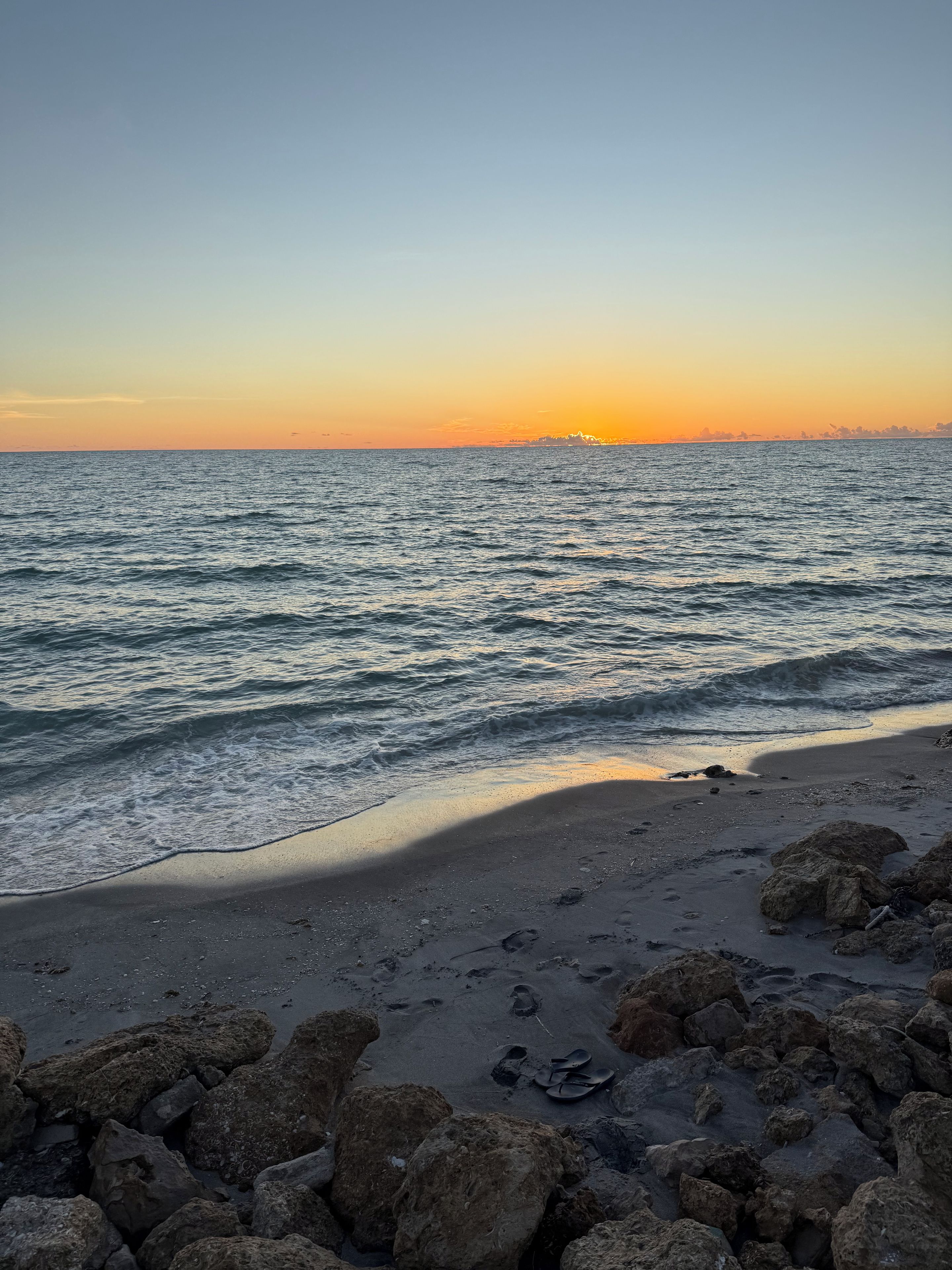 Une plage avec des vagues, un coucher de soleil et des rochers éparpillés.