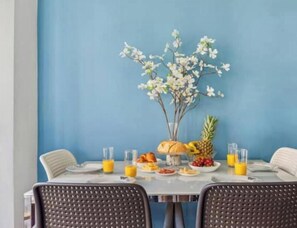 Une table à manger avec des assiettes remplies de nourriture, des verres de jus d’orange et un vase contenant des fleurs blanches.