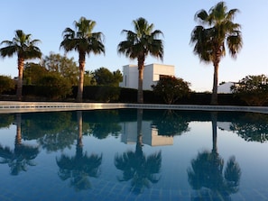 A swimming pool with clear reflections of palm trees and a modern building in the background. - Holiday Home With 2 Bedrooms (Campos)