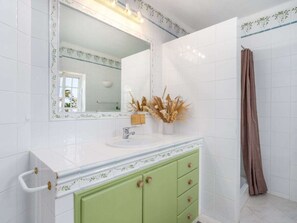 Ein Badezimmer mit weißen Fliesen, einem grünen Waschtisch und einer Duschvorhang.
