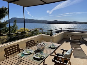 An outdoor dining area with a table set for two, overlooking a body of water and hills. - Villa Grand Bleu (La Seyne-sur-Mer)