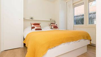 A bedroom with a bed, a window, and a white wall.
