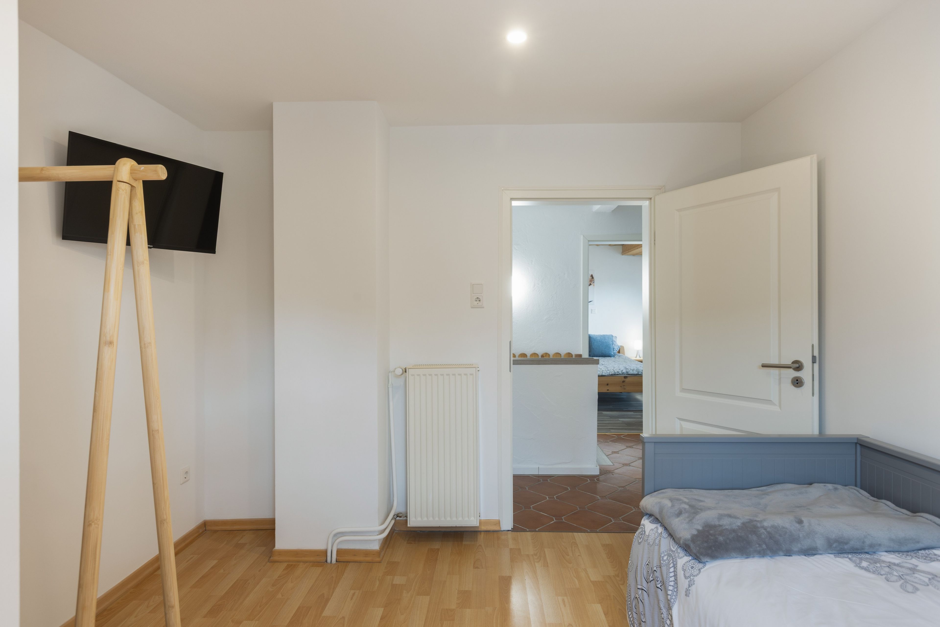 Ein Schlafzimmer mit einem Bett, Holzboden, Heizkörper und einem an der Wand befestigten Fernseher.