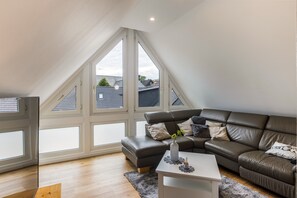 Ein modernes Schlafzimmer im Loft-Stil mit schrägem Dach, großen Fenstern, einem Ledersofa und einem kleinen weißen Tisch.