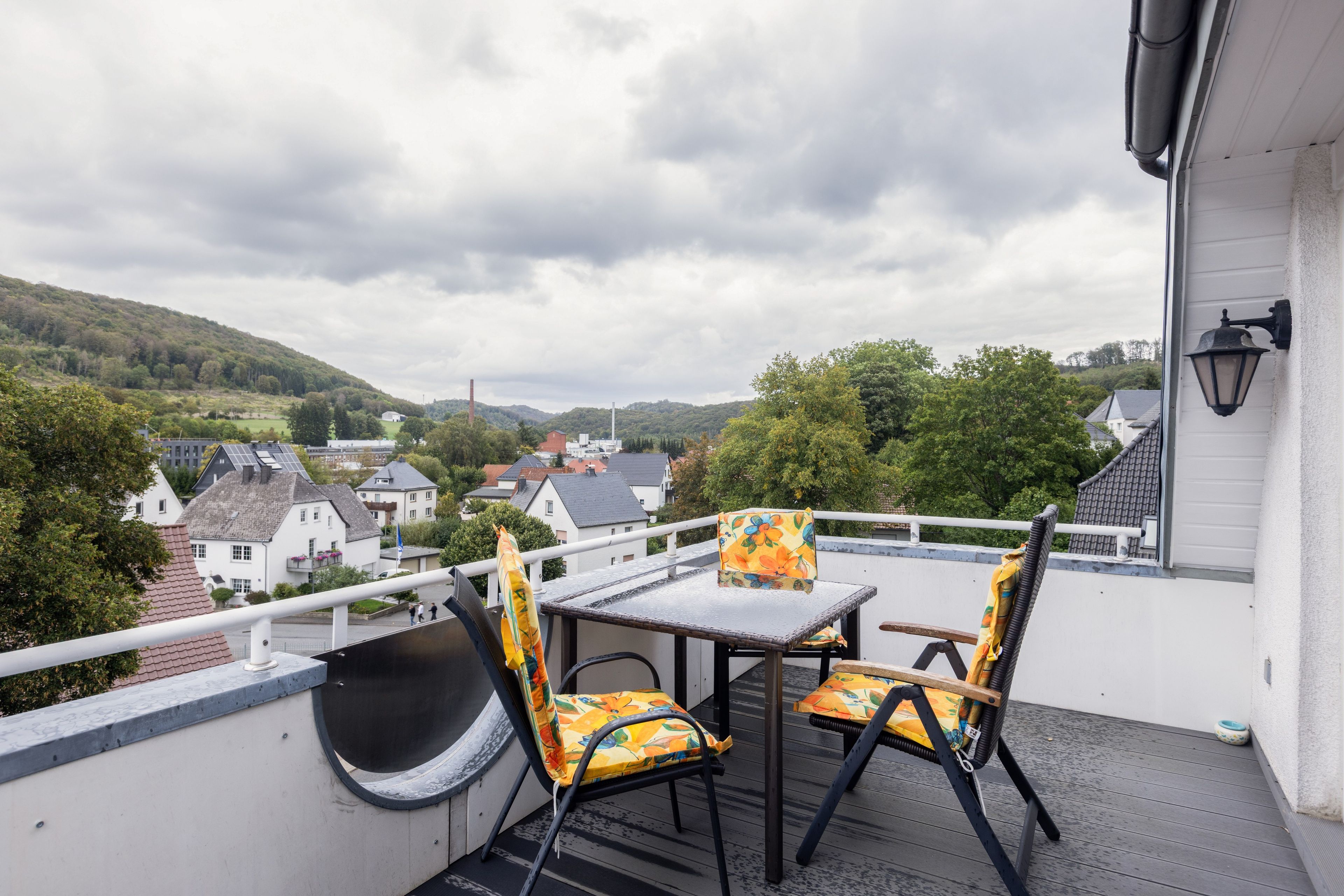 Ein Balkon mit Tisch und Stühlen, der auf einen Wohnbereich mit Häusern und einen Hügel blickt.