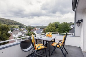 Een balkon met een tafel en stoelen, met uitzicht op een woonwijk met huizen en een heuvel.