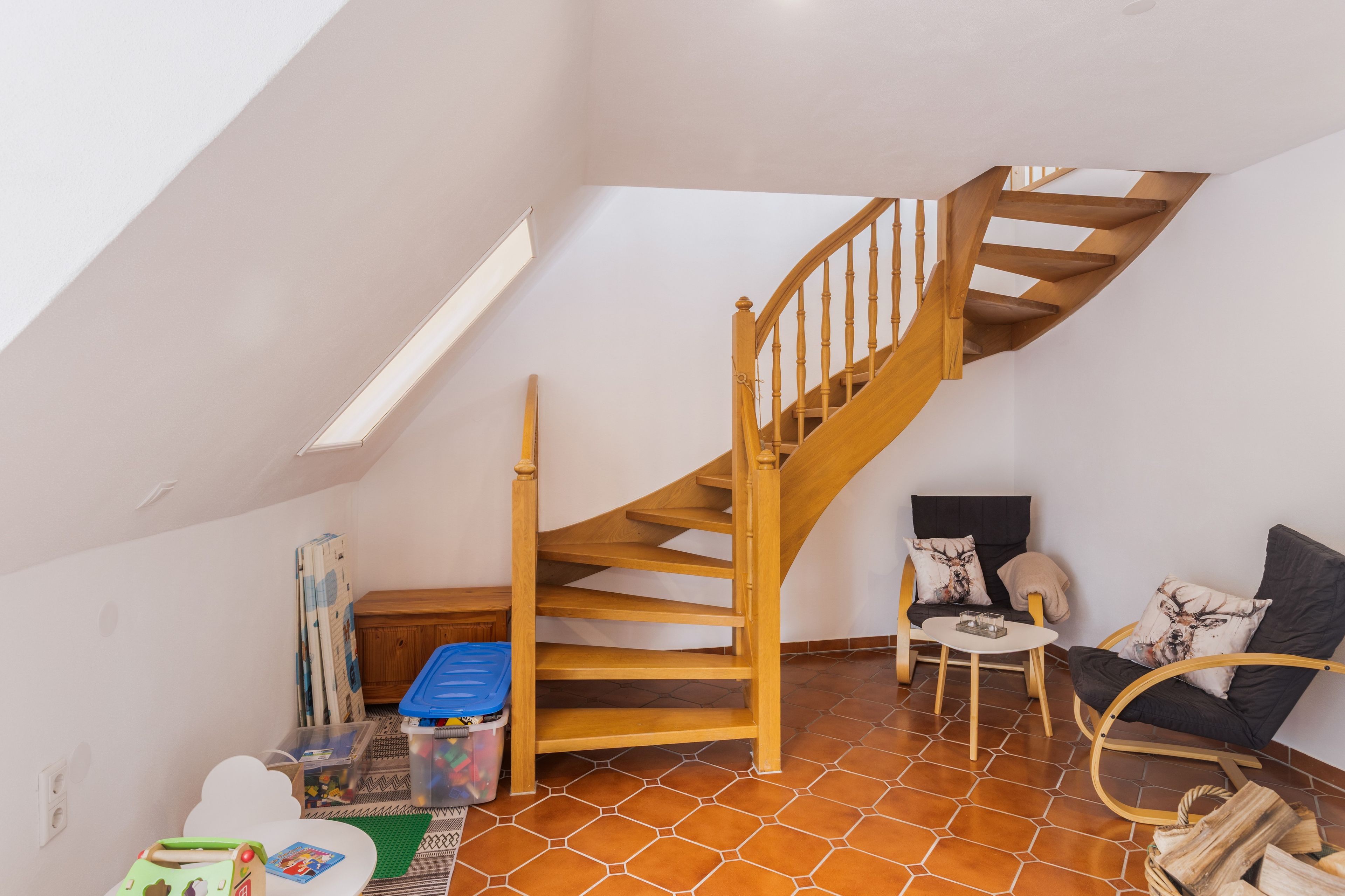 Ein Zimmer mit einer Wendeltreppe aus Holz, einem kleinen runden Tisch mit einer Kerze und einem Stuhl mit Kissen.
