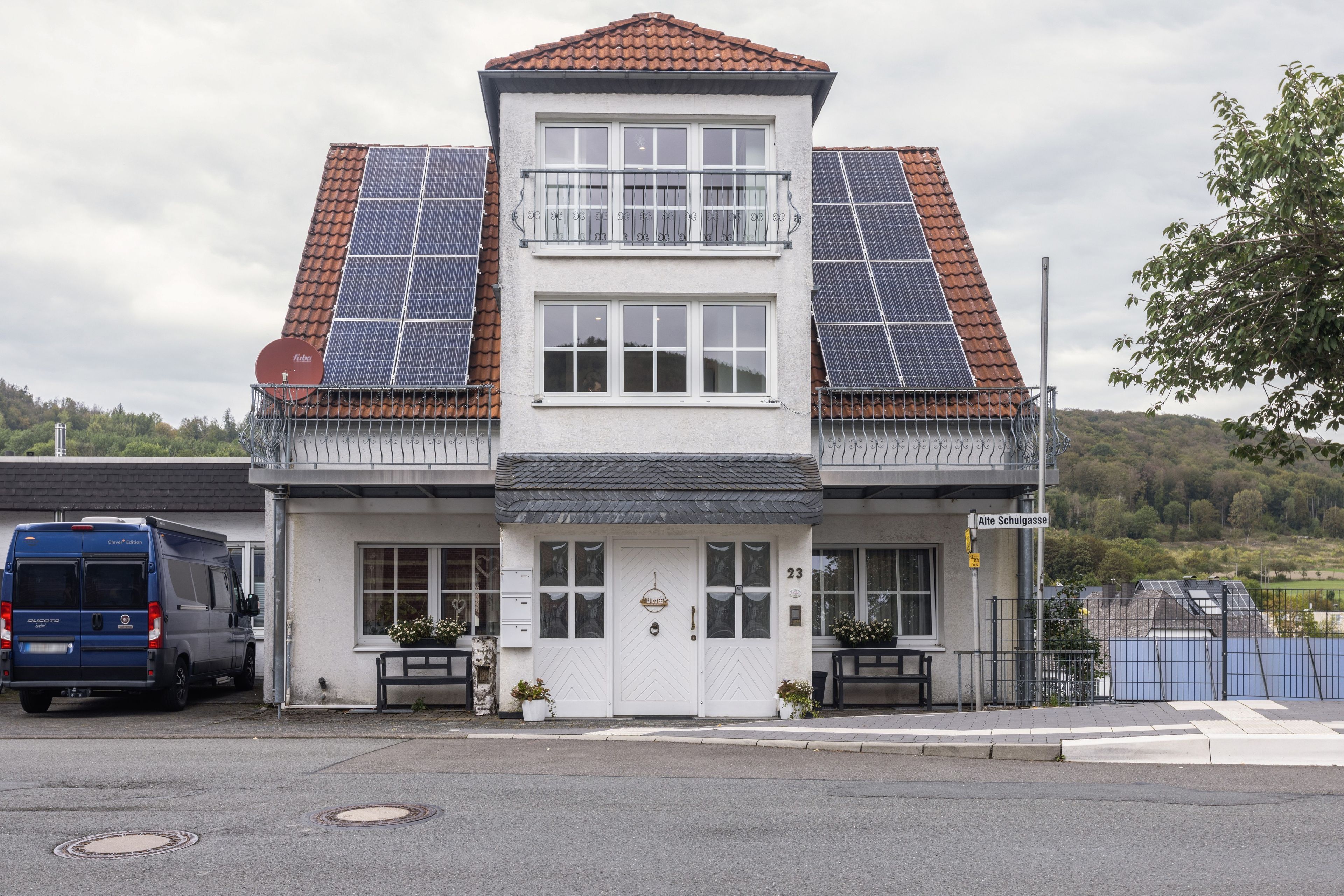 Une maison à deux étages avec des panneaux solaires sur le toit, un garage et une vue sur la rue.